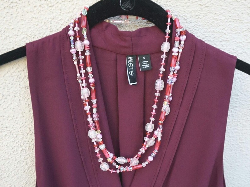 May include: A multi-strand necklace with pink, red, and clear beads. The necklace is layered and has a variety of bead shapes and sizes.