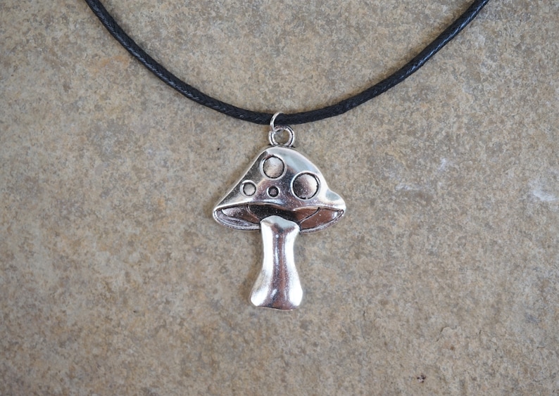 Puede incluir: Un collar con un colgante de hongo plateado en un cord&oacute;n de cuero negro.
