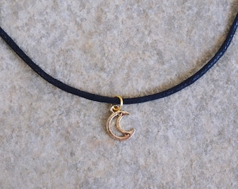 Puede incluir: Un collar choker negro simple con un dije de media luna de oro.