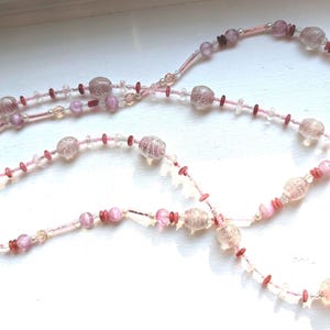 May include: A long pink and white beaded necklace with a silver clasp. The beads are various sizes and shapes, including round, oval, and teardrop.