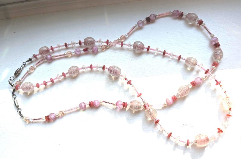 May include: A long pink and white beaded necklace with a silver clasp. The beads are various sizes and shapes, including round, oval, and teardrop.