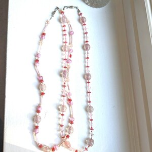 May include: Two layered necklaces with pink and red glass beads. The beads are clear with a subtle sparkle and have a textured surface.