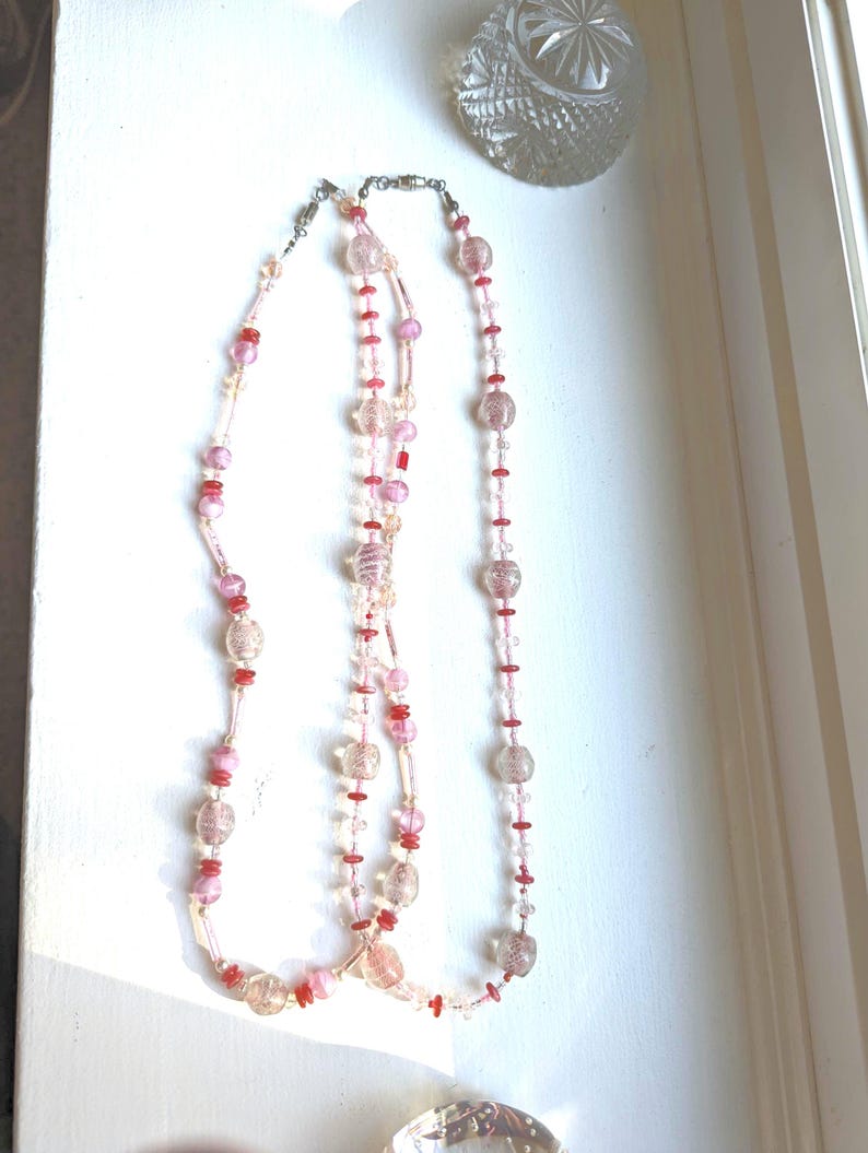 May include: Two layered necklaces with pink and red glass beads. The beads are clear with a subtle sparkle and have a textured surface.