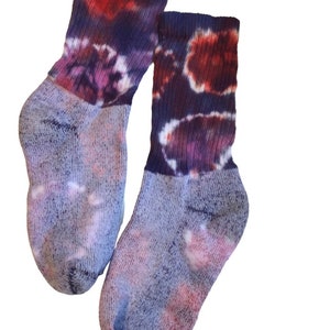 May include: A pair of tie-dye socks in shades of purple, blue, and red. The socks have a white background with a tie-dye pattern.