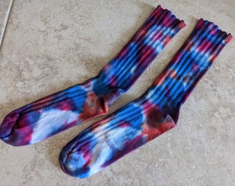 Puede incluir: Un par de calcetines tie-dye en tonos de azul, rojo y blanco. Los calcetines tienen una textura acanalada y están hechos de un material suave y cómodo.