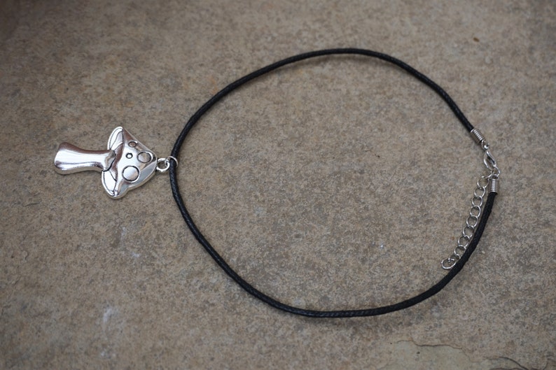 Puede incluir: Un collar con un colgante de hongo plateado, un cord&oacute;n negro y un cierre plateado.