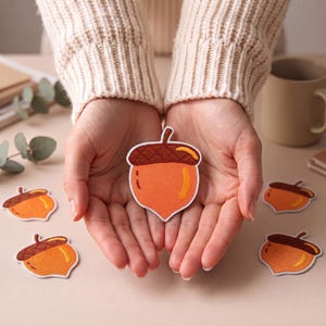 Peut inclure: Un écusson brodé en forme de gland avec un fruit orange vif, un chapeau texturé marron foncé et une bordure blanche. L'écusson présente une finition cousue lisse et une forme de gland classique avec une petite tige au sommet.