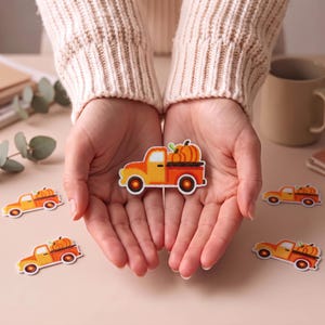 Puede incluir: Un parche bordado que muestra una camioneta vintage de color naranja que transporta una calabaza grande de color naranja en su caja. El parche tiene un borde blanco y está diseñado con hilos de colores naranja, amarillo y marrón vibrantes.