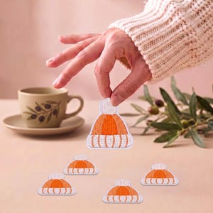 May include: Five embroidered patches shaped like winter beanies with orange and white striped patterns and a white pom-pom on top. Each patch features a ribbed cuff design and a rounded crown, rendered in detailed thread work with a white border.
