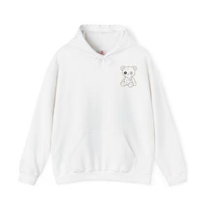 Könnte beinhalten: Ein weißer Kapuzenpullover mit langen Ärmeln und einer kleinen schwarz-weißen Strichzeichnung eines Teddybären auf der linken Brust. Der Bär hat ein schwarzes Auge, ein knopfartiges Auge und ein aufgesticktes Herz auf der Brust. Mit Fronttasche.