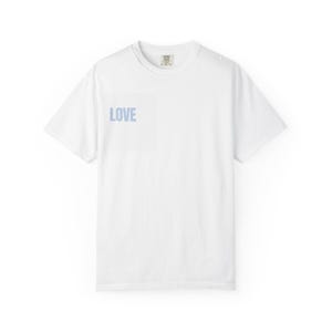 Può includere: Una t-shirt bianca a maniche corte con la parola LOVE stampata in azzurro sul lato sinistro del petto. Il capo presenta un girocollo e una vestibilità standard, con una piccola etichetta del marchio visibile all'interno del colletto.