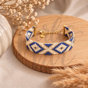 May include: A woven bead bracelet featuring a geometric diamond pattern in royal blue, cream, and gold. The bracelet includes gold-toned metal end caps, a delicate chain extender, and a small circular charm, creating a structured and detailed accessory.