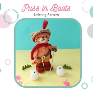 Puede incluir: Una muñeca de punto de Gato con Botas con una capa roja, botas marrones y un sombrero marrón con una pluma roja. La muñeca sostiene un palo y está de pie sobre una superficie amarilla con dos ratones blancos.