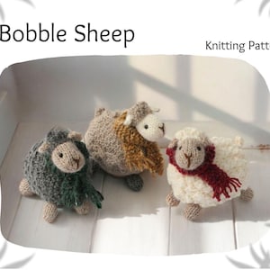 Puede incluir: Tres pequeños juguetes de oveja tejidos a mano con cuerpos texturizados de punto bobble. Las ovejas son de color gris oscuro, marrón claro y crema, cada una con una pequeña bufanda tejida en verde oscuro, marrón o rojo. El texto dice Bobble Sheep Knitting Pattern.