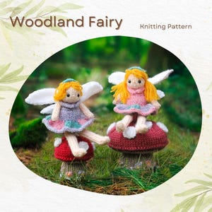 May include: Two knitted woodland fairy dolls with wings, sitting on mushroom-shaped bases. The fairies are wearing pink and purple dresses with white wings. The mushrooms are red and white with green moss at the base. The background is a blurred image of green foliage.