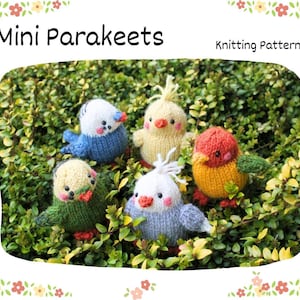 May include: A knitting pattern titled Mini Parakeets featuring five small, colourful, hand-knitted bird figures. The birds are crafted in shades of blue, yellow, red, green, and white, each with small black eyes, orange beaks, and pink cheeks.