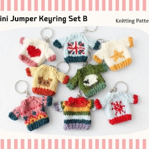 Può includere: Una collezione di otto portachiavi a forma di mini maglioni lavorati a maglia con l'etichetta Mini Jumper Keyring Set B Knitting Pattern. Ogni piccolo maglione presenta motivi distinti tra cui un cuore rosso, una bandiera, una stella, una pecora e vari disegni colorati.