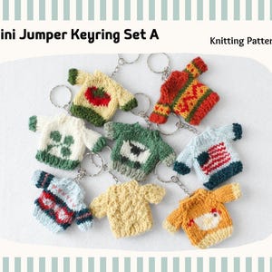 Könnte beinhalten: Eine Sammlung von acht gestrickten Mini-Pullover-Schlüsselanhängern mit verschiedenen Mustern wie Tomate, Schaf, Flagge und Huhn. Der Text Mini Jumper Keyring Set A und Knitting Pattern ist oben zu sehen. Jeder Pullover hat einen Metallring.