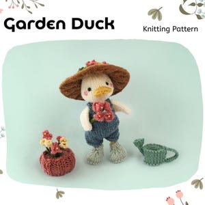 Op de afbeelding: Een gebreide Tuineend met een bruine hoed en blauwe overall, met een bloempot en een gieter. De eend heeft een gele snavel en is omgeven door een lichtgroene achtergrond. De tekst "Garden Duck" en "Knitting Pattern" zijn zichtbaar.