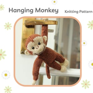 Puede incluir: Un juguete de mono marrón tejido colgado de un pomo de la puerta. El mono tiene una cara beige con ojos negros y una nariz marrón. El juguete es un patrón de tejido.