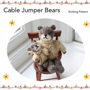 May include: Knitting pattern for two cable jumper bears. A larger brown bear is sitting on a wooden chair, holding a smaller beige bear. The bears are wearing knitted sweaters.