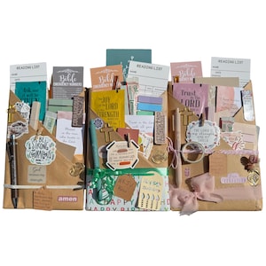 May include: Three brown paper gift envelopes filled with religious stationery, including reading lists, pens, small cross charms, and cards with inspirational text like Be Strong and Courageous, The Joy of the Lord, and Trust in the Lord.