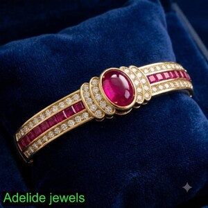 May include: A gold hinged bangle bracelet featuring a central oval cabochon ruby surrounded by small round diamonds. The band is accented with rows of square-cut rubies and round diamonds. The text "Adelide jewels" appears in the bottom corner.