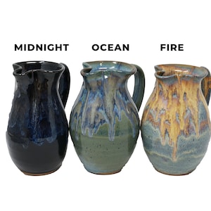 May include: Three ceramic pitchers in Midnight, Ocean, and Fire colors. The Midnight pitcher is dark blue, the Ocean pitcher is blue and green, and the Fire pitcher is yellow and blue. Each pitcher has a handle and a unique, wavy rim.