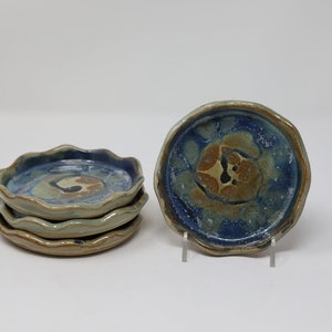 May include: Set of four small, scalloped ceramic dishes with a blue, brown, and white glaze. The dishes are stacked on top of each other.