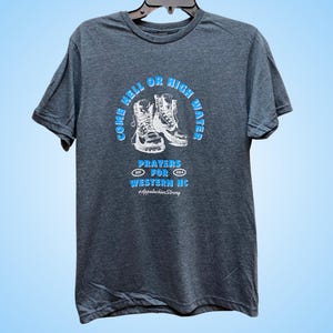 Puede incluir: Una camiseta gris oscuro con un gr&aacute;fico blanco de dos botas de senderismo y el texto "Come Hell or High Water, Prayers for Western NC, #AppalachianStrong".