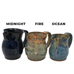 Op de afbeelding: Drie keramische kannen in verschillende kleuren: middernachtblauw, groen met bruine accenten en blauw met bruine accenten. De kannen zijn gelabeld met "Middernacht", "Vuur" en "Oceaan".