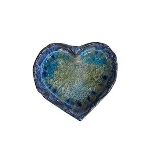 以下が含まれることがあります： ひび割れた質感のハート型のセラミック皿。 青と緑の色合いのグラデーションがあり、濃い青色の縁と金色のトリムが付いています。エッジはスカラップのデザインです。