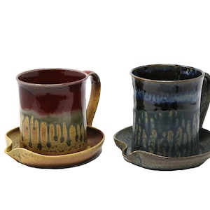 May include: Two ceramic mugs with matching saucers. The mug on the left is red with a yellow and brown drip glaze. The mug on the right is blue with a yellow and brown drip glaze.
