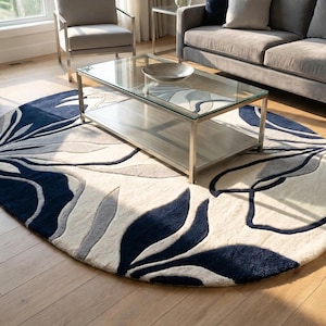 May include: A large circular area rug featuring a bold, abstract floral pattern in deep navy blue, light gray, and cream. The design consists of sweeping, organic leaf-like shapes that curve across the surface, creating a high-contrast visual effect.