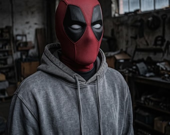 Op de afbeelding: Een rood en zwart gestructureerd masker dat het hele hoofd bedekt met witte ooglenzen, gedragen met een grijze hoodie met lange mouwen. Het masker heeft een opvallend mesh-achtig stofpatroon en zwarte oogvlakken, gecombineerd met een grijze hoodie.
