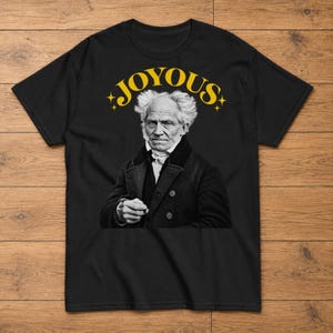 Könnte beinhalten: Ein schwarzes T-Shirt mit kurzen Ärmeln und einem Grafikdruck einer historischen Persönlichkeit mit wildem Haar und dunklem Mantel. Über der Figur steht das Wort JOYOUS in einer fetten gelben Serifenschrift, flankiert von kleinen Sternen.