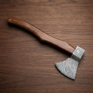 May include: A hand axe featuring a curved dark brown wooden handle and a sharp metal head with a distinct wavy Damascus steel pattern. The handle includes a small circular metal pin near the end, and the blade is securely attached to the wood.
