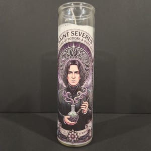 May include: A tall cylindrical glass prayer candle featuring a white wax core and a label with a purple-toned illustration of a man with dark hair holding a potion flask. The text reads SAINT SEVERUS, OUR LORD OF POTIONS & DARK ARTS, and ALWAYS.