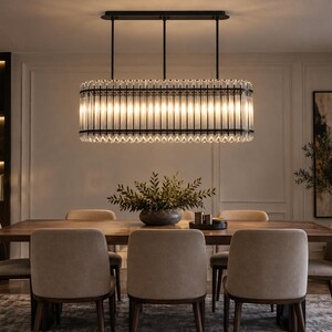 May include: A rectangular chandelier featuring a black metal frame and vertical clear glass rods. The fixture is suspended by three thin black rods from a rectangular black ceiling mount, emitting a warm glow through the glass elements.