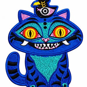 Puede incluir: Un parche bordado que muestra un gato azul con rayas negras, grandes ojos amarillos con iris rojos y una amplia sonrisa que muestra dientes blancos afilados. El gato lleva un sombrero de copa negro con una pluma amarilla y un ojo blanco.
