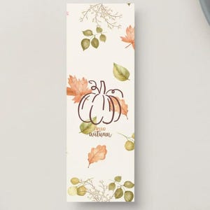 May include: A rectangular bookmark with a cream background featuring a brown line-art pumpkin at the center. The text "hello autumn" is printed below the pumpkin. The design includes scattered watercolor-style orange and green leaves.