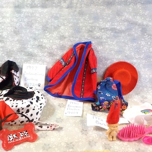 May include: A collection of doll accessories, including a red coat with blue trim, a Dalmatian-themed hat and purse, a red hat, and a blue floral bag. There is also a small troll doll with a red wig and a pink brush.