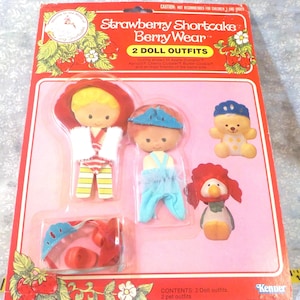 May include: A vintage Strawberry Shortcake Berry Wear doll outfit set in its original packaging. The set includes two doll outfits and two pet outfits. The packaging is red and features the Strawberry Shortcake logo and illustrations of strawberries and flowers.