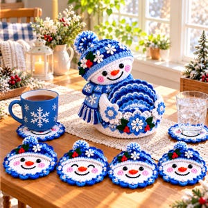 May include: A crochet snowman-shaped coaster holder with a matching blue and white scarf and pom-pom hat, containing several round snowman face coasters. The set features blue and white yarn, snowflake accents, and small red berry details.