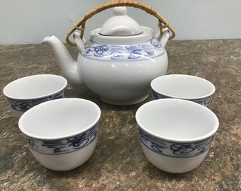 May include: A white teapot with a blue and white floral design and a bamboo handle, along with four matching teacups.