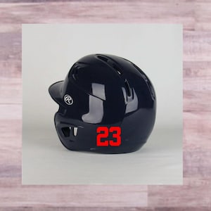 May include: A navy blue baseball helmet with a white logo and the number 23 in red.
