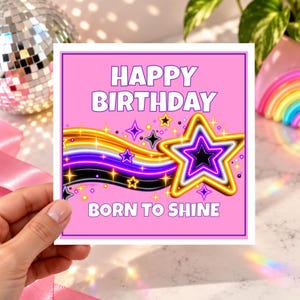 May include: A square greeting card with a pink background featuring the text HAPPY BIRTHDAY and BORN TO SHINE in white. A graphic of a large star with yellow, white, and black outlines sits next to a wavy trail of yellow, white, and black lines.