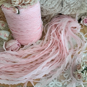 May include: A spool of light pink lace ribbon with a delicate floral design. The ribbon is surrounded by loose strands of the same lace, along with decorative roses and other lace trimmings. This image is ideal for craft projects.