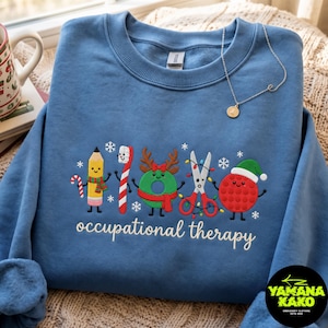 May include: A blue crewneck sweatshirt featuring embroidered holiday-themed occupational therapy icons including a pencil, toothbrush, wreath, scissors, and sensory ball, with the text "occupational therapy" in white script lettering.