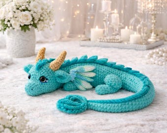 May include: A turquoise crochet dragon plush toy featuring two textured golden horns, small layered wings with white and light blue accents, and a long curled tail. The creature has large dark eyes with blue highlights and a soft yarn texture.
